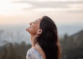 Serene outdoor portrait of a smiling woman enjoying the sunset in a peaceful landscape.
