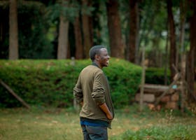 A young man smiling and enjoying a peaceful moment in a lush outdoor park with greenery.
